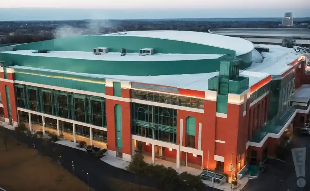 Aerial view of a large, modern stadium with a green roof and red brick exterior.