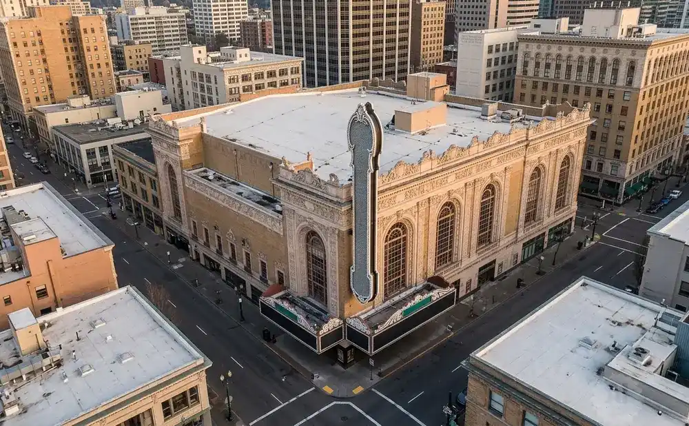 Aerial view of a grand, ornate theater with a large marquee, surrounded by city buildings.
