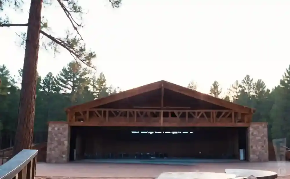 Outdoor wooden amphitheater with stone accents, surrounded by pine trees.