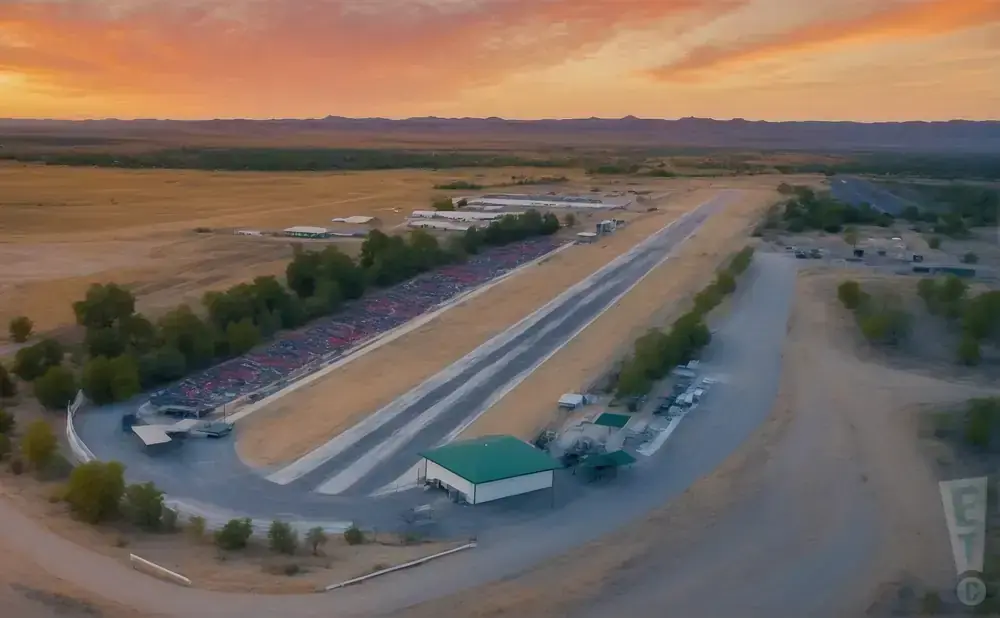 Aerial view of a drag strip with bleachers, a building, and a sunset sky.