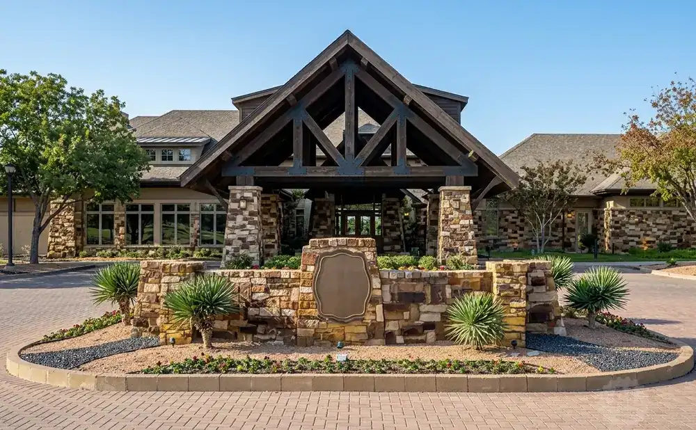 A stone building with a wooden covered entrance and a circular paved driveway in front.