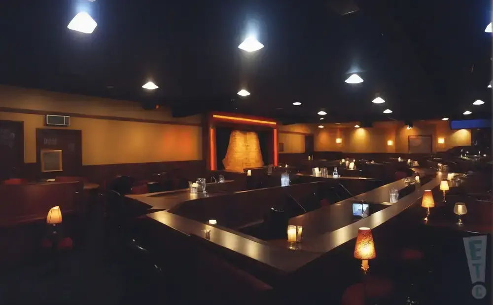 Dimly lit comedy club with rows of tables and a stage area.