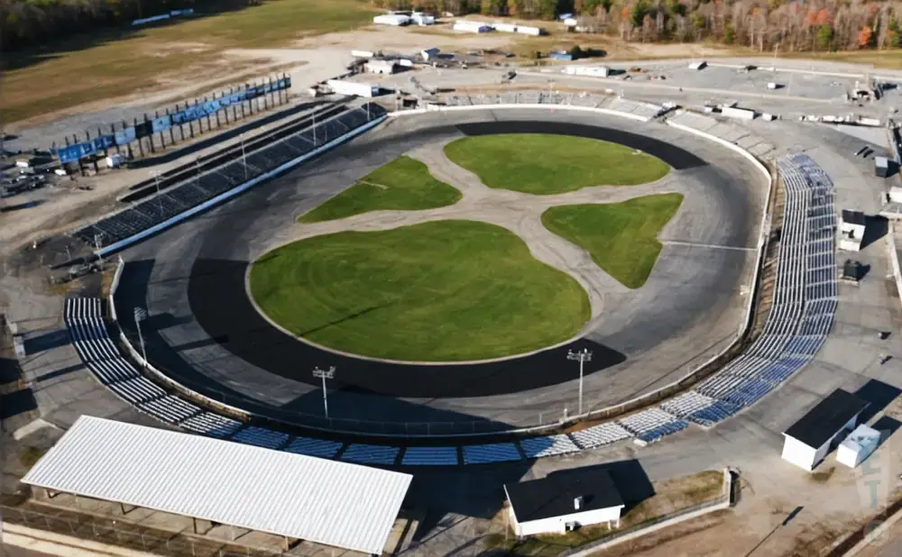 Aerial view of a race track with grandstands, a green infield, and surrounding buildings.