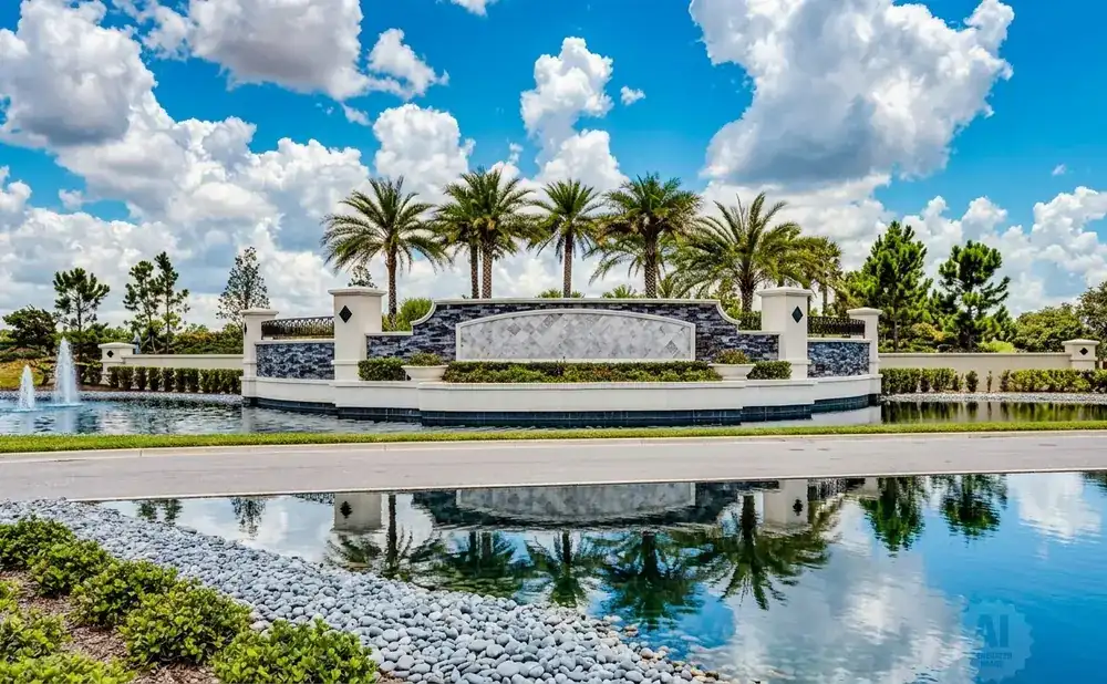 Entrance to a community with palm trees, fountains, and a reflective pond.
