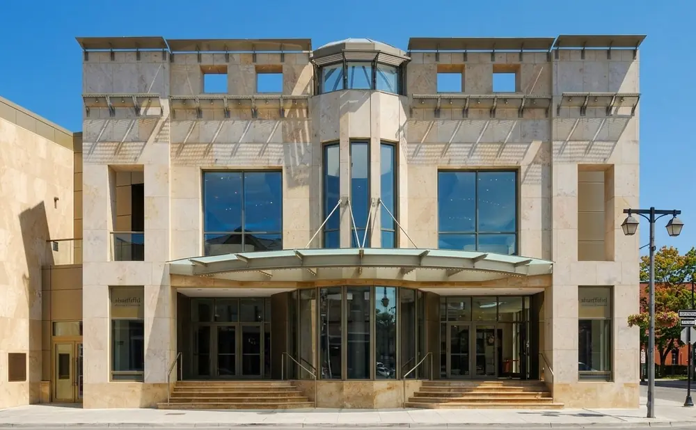 Modern stone building with large glass windows and doors under a metal awning.