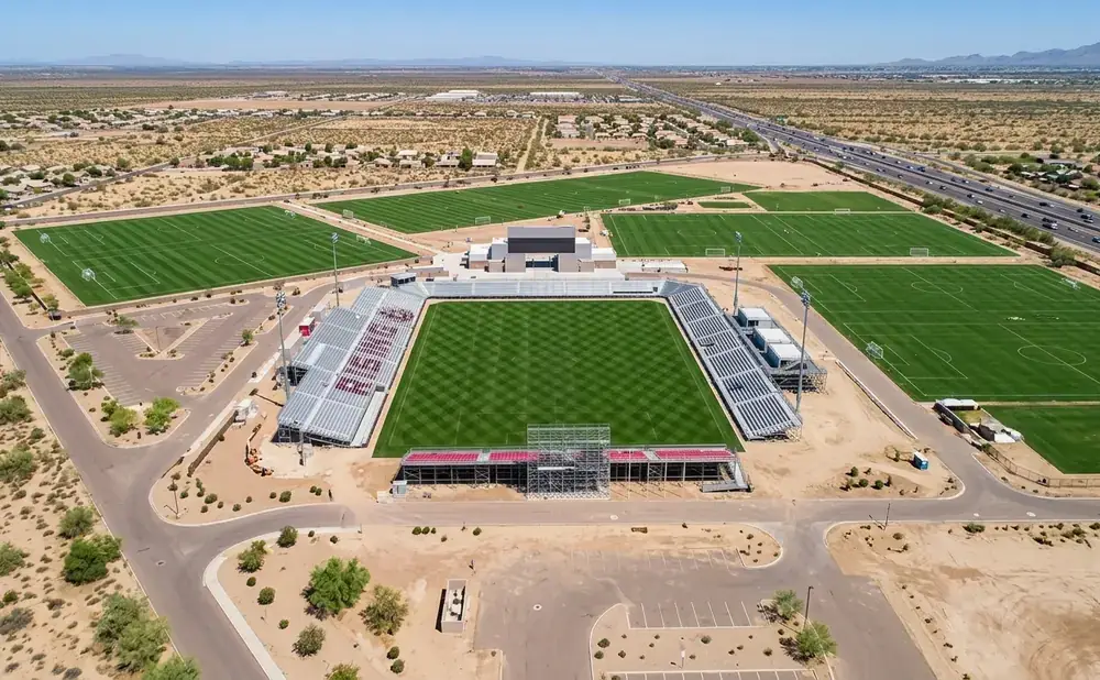 Aerial view of a soccer stadium with multiple practice fields and surrounding desert landscape.
