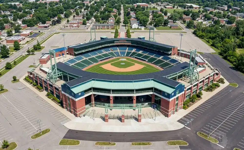 Aerial view of a baseball stadium with empty parking lots and surrounding residential areas and trees.