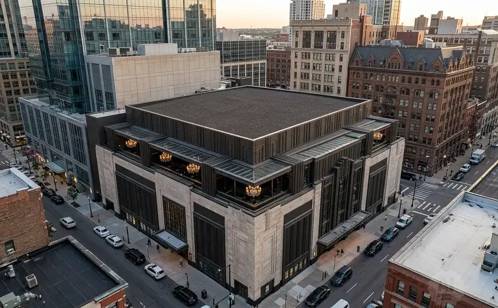 Aerial view of a modern building with a flat roof, surrounded by city buildings and streets with cars.