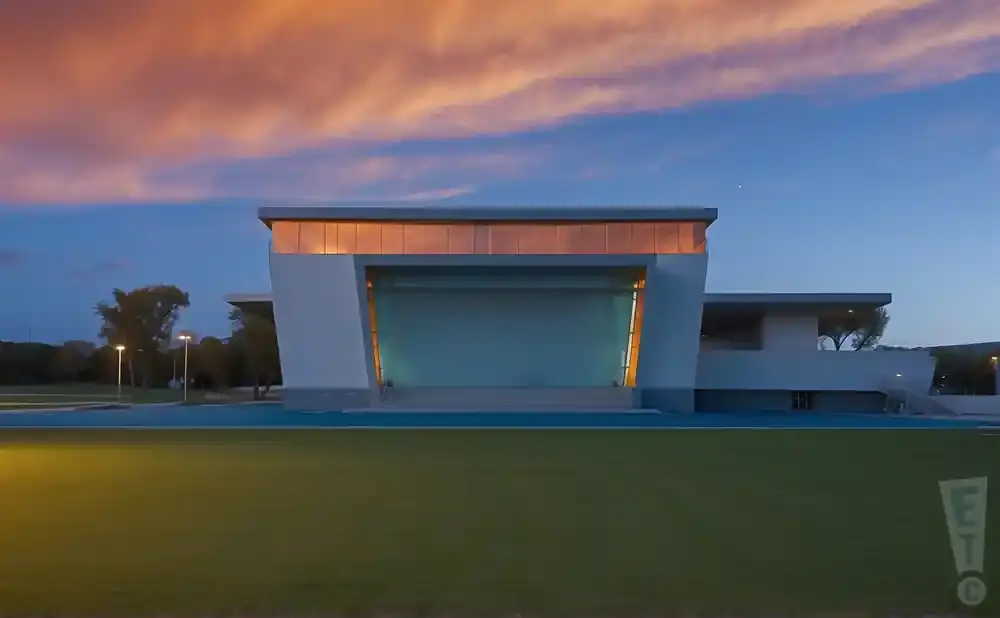 Modern white building with a glass stage front, against a sunset sky.