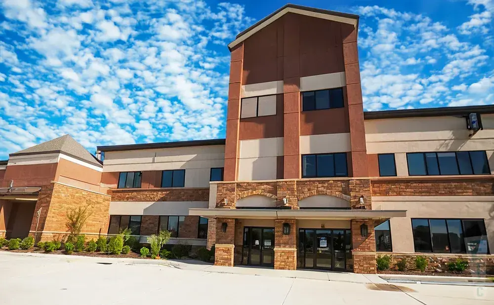Modern building with stone accents and a red and tan facade under a blue, cloudy sky.
