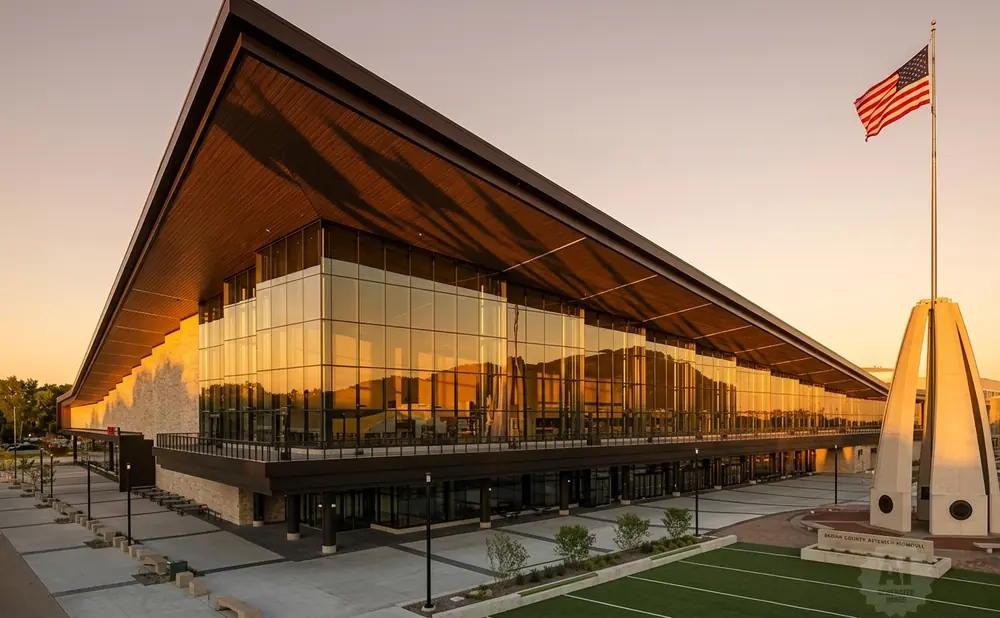 Modern building with glass facade and overhanging roof, flying American flag at sunset.