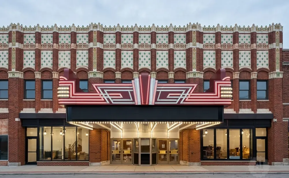 Art Deco theater marquee with red and white neon lights above a brick building facade with decorative tile work.