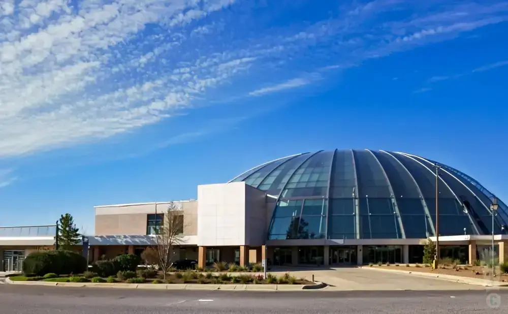 Modern building with a large glass dome roof under a blue sky with scattered clouds.