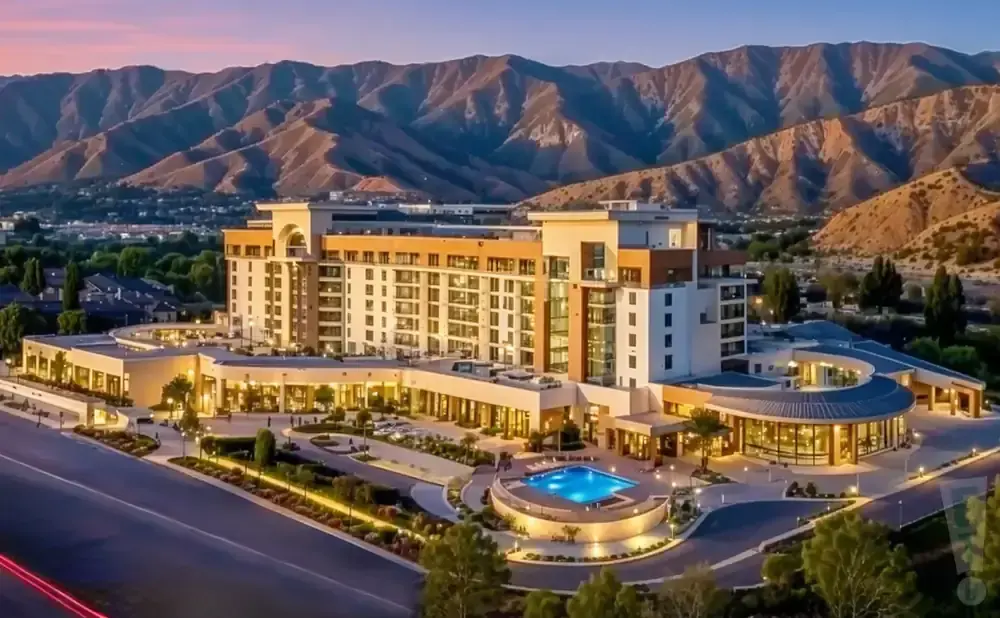 An aerial view of a modern hotel with a pool and mountains in the background at sunset.