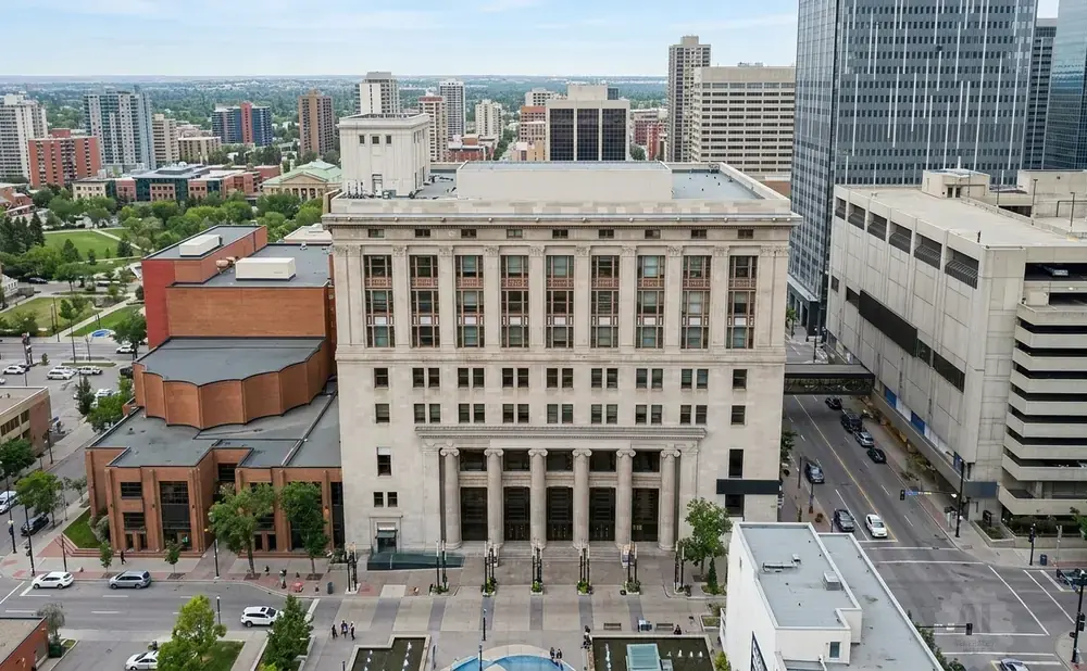 Aerial view of a grand stone building with columns, surrounded by other city buildings and green spaces.