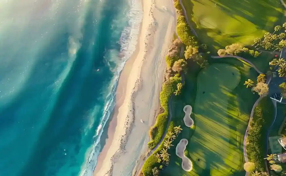 Aerial view of a beach and golf course with turquoise water and lush green fairways.