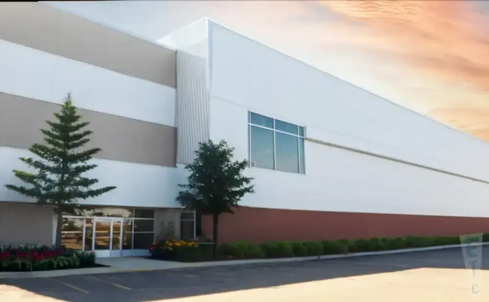 Modern industrial building with large white panels, a red base, and a large window.