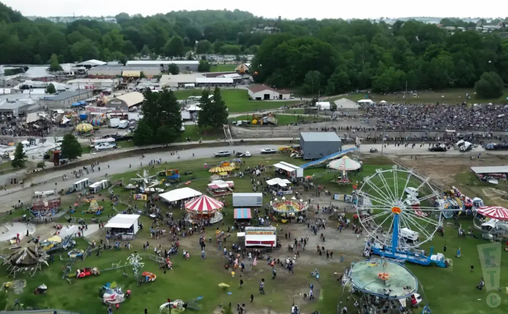 Aerial view of a crowded outdoor fair with rides, tents, and food vendors.