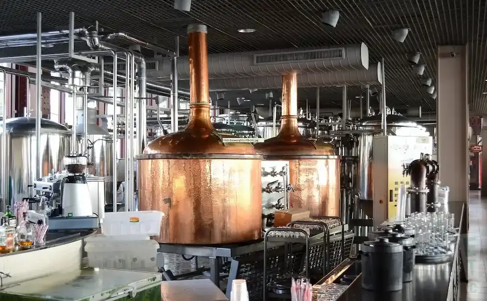 Brewery interior with copper tanks, brewing equipment, and a bar with glasses.