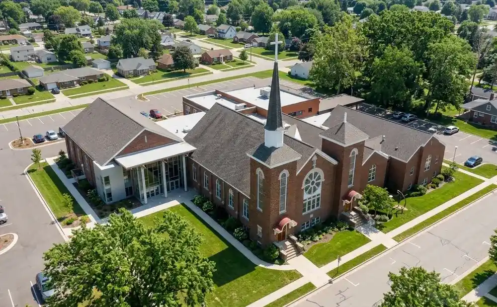 Aerial view of a brick church with a steeple and modern addition, surrounded by a suburban neighborhood and trees.