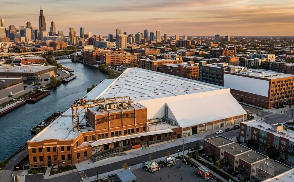 Aerial view of a triangular building with a white roof next to a river in an urban setting.