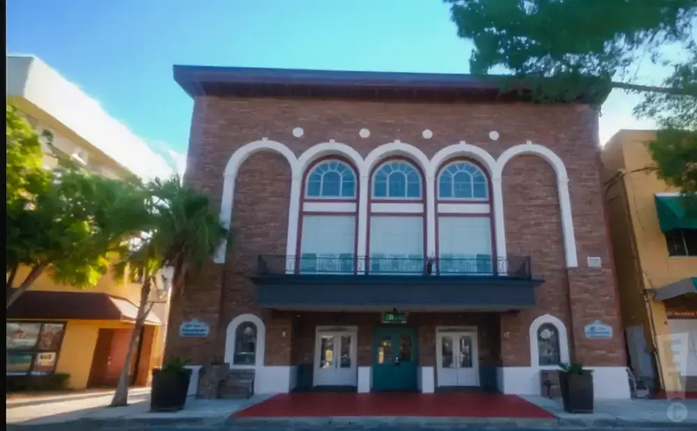 A brick building with arched windows and a red carpet leading to its entrance.