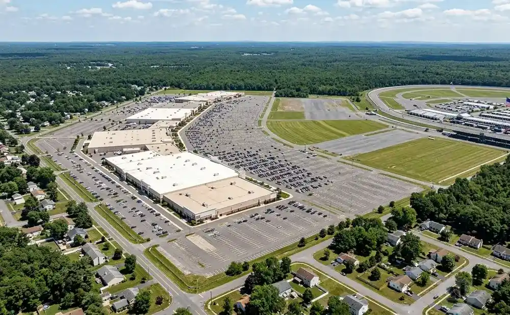Aerial view of a large retail complex with a vast parking lot and a race track in the background.
