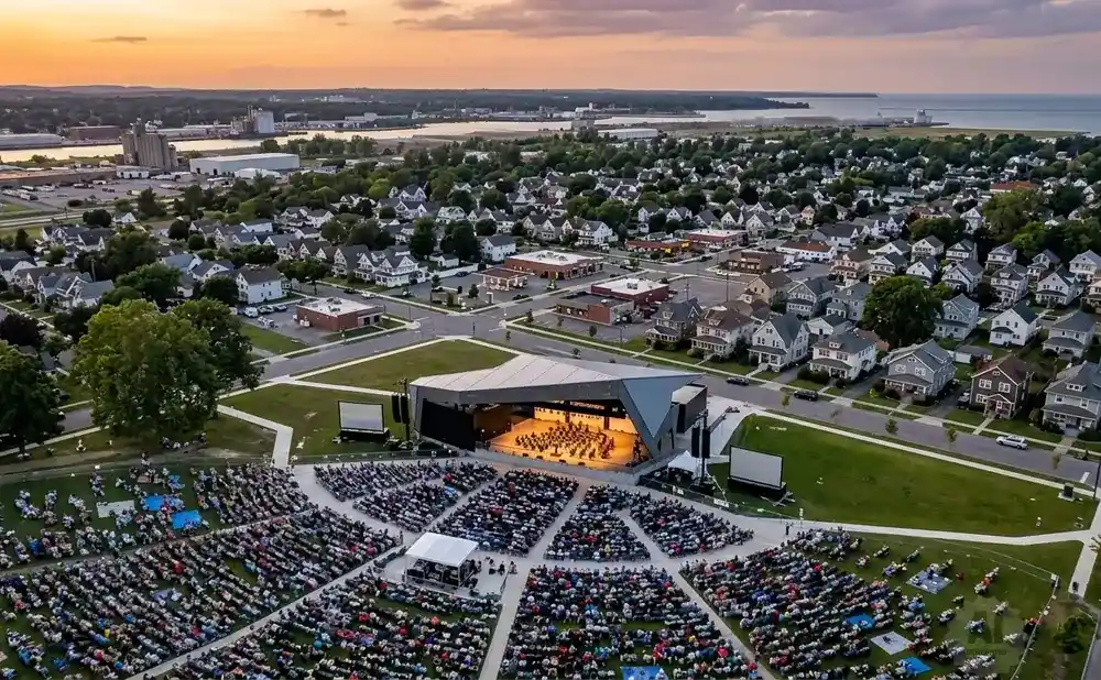 Aerial view of an outdoor concert with a large audience and orchestra on stage.