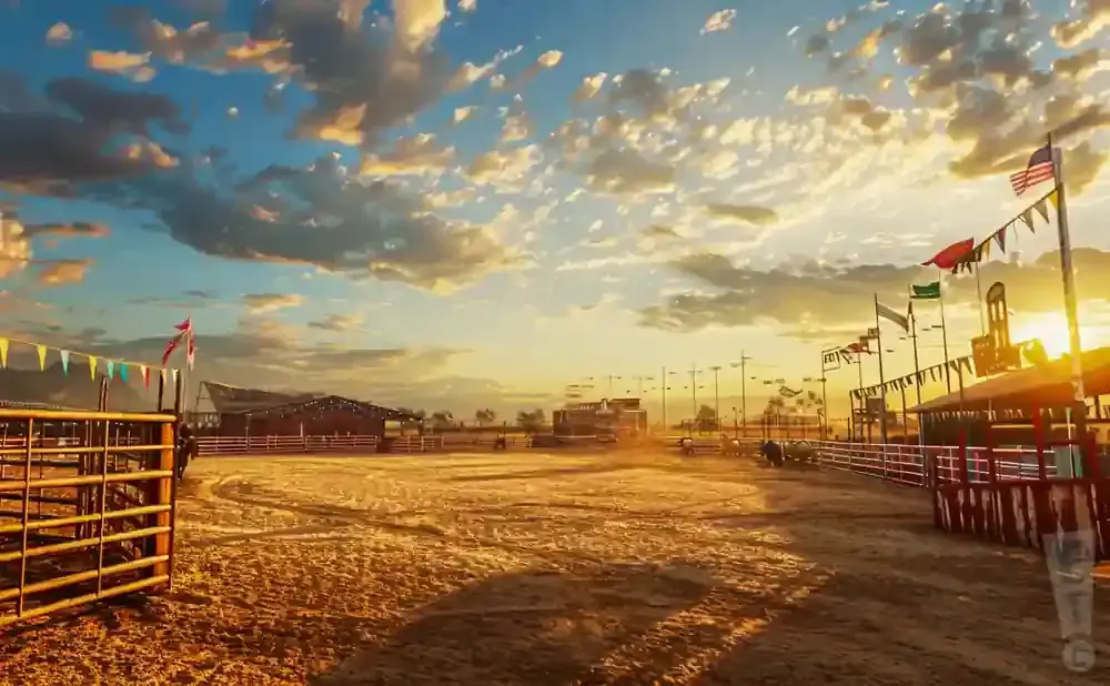 Rodeo arena at sunset with colorful flags and dramatic clouds.