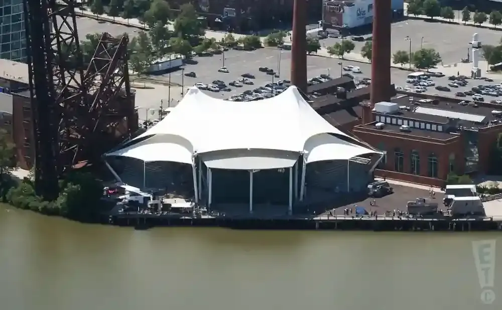 An outdoor concert venue with a white tent structure on a pier beside a body of water.