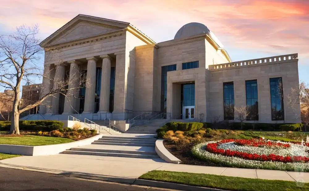 A grand stone building with columns, a dome, and a flower garden.