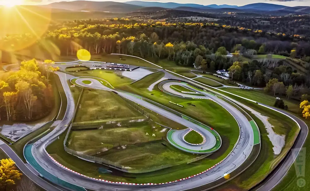 Aerial view of a winding race track surrounded by trees and hills during golden hour.