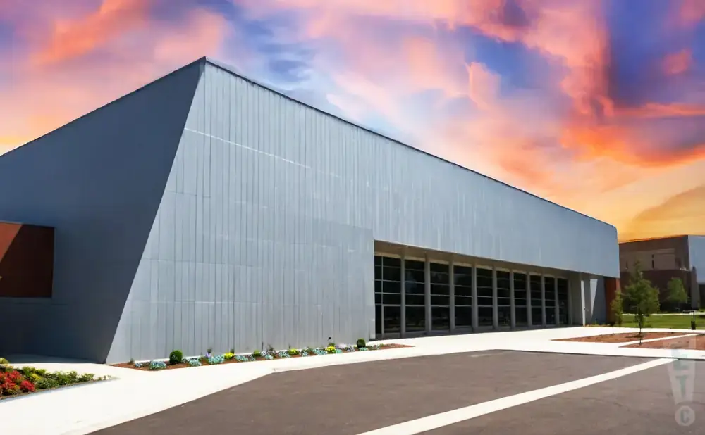 Modern building with a gray facade and large windows under a colorful sunset sky.