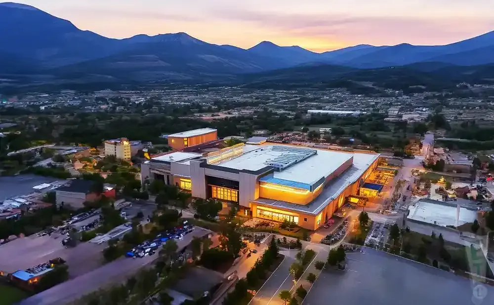 Aerial view of a large, brightly lit building at dusk with mountains in the background.