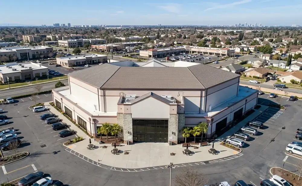 Aerial view of a large, multi-sided building with a prominent entrance, surrounded by parking lots and residential areas.