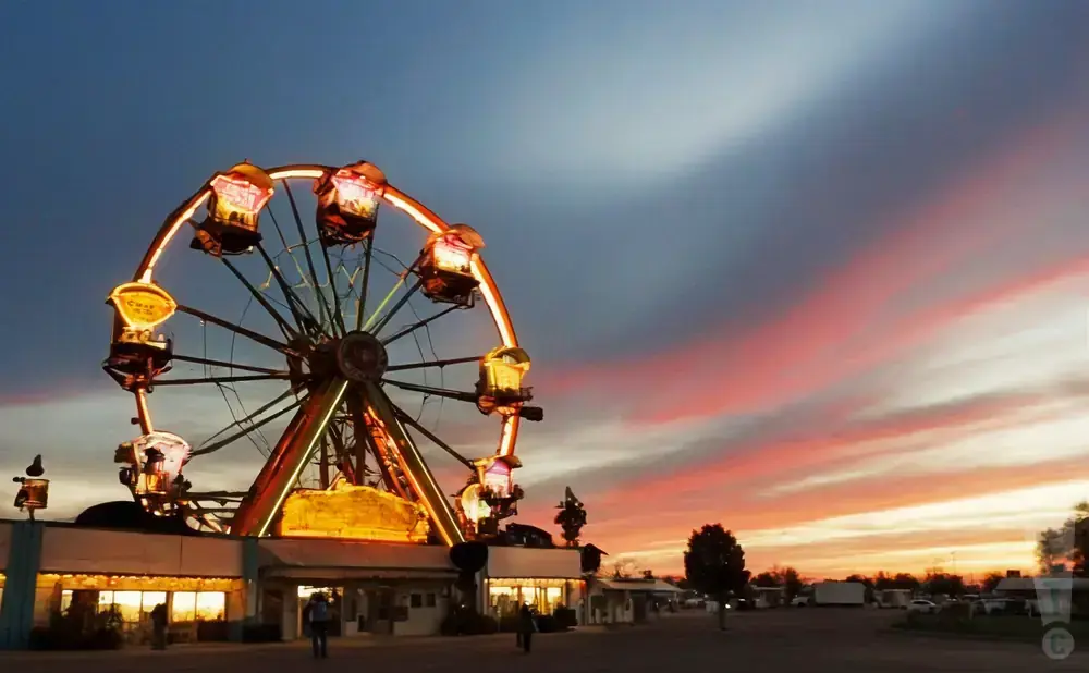 A Ferris wheel is lit up against a dramatic sunset sky with pink and orange clouds.