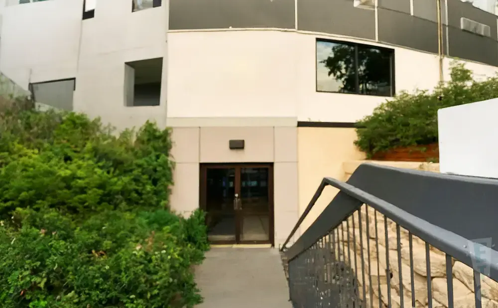 A modern building with lush green bushes and a set of double glass doors.