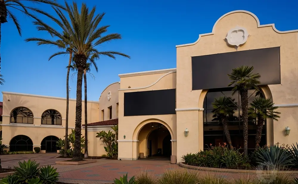 Spanish-style building with palm trees and large black screens.
