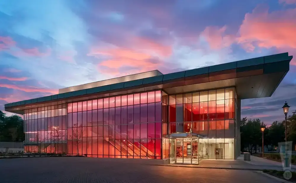 Modern glass building with red interior lighting during a colorful sunset.