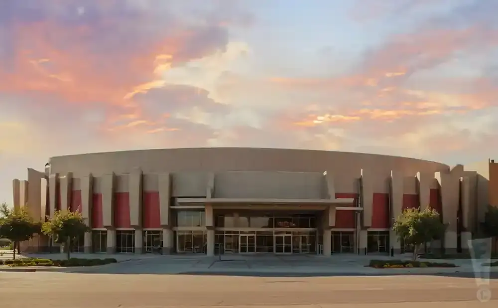 A large, modern building with a curved facade and red accents under a sunset sky.