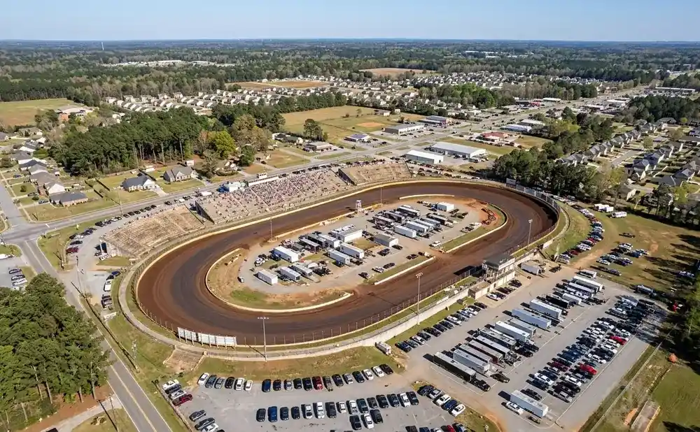 Aerial view of a dirt oval racetrack with grandstands, parking lots, and surrounding neighborhoods.