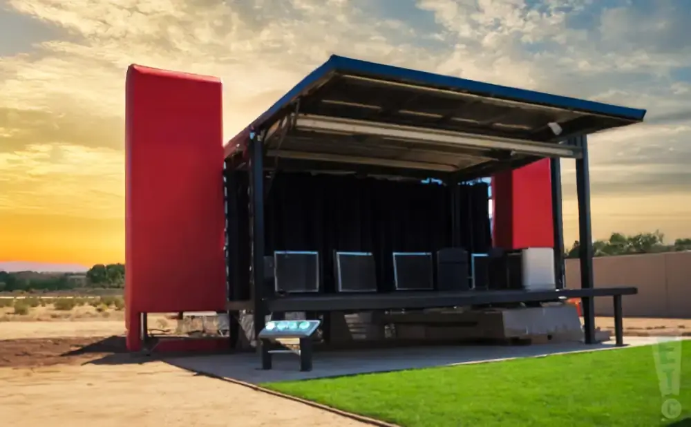 A portable stage with red side panels and black curtains, set against a sunset sky.