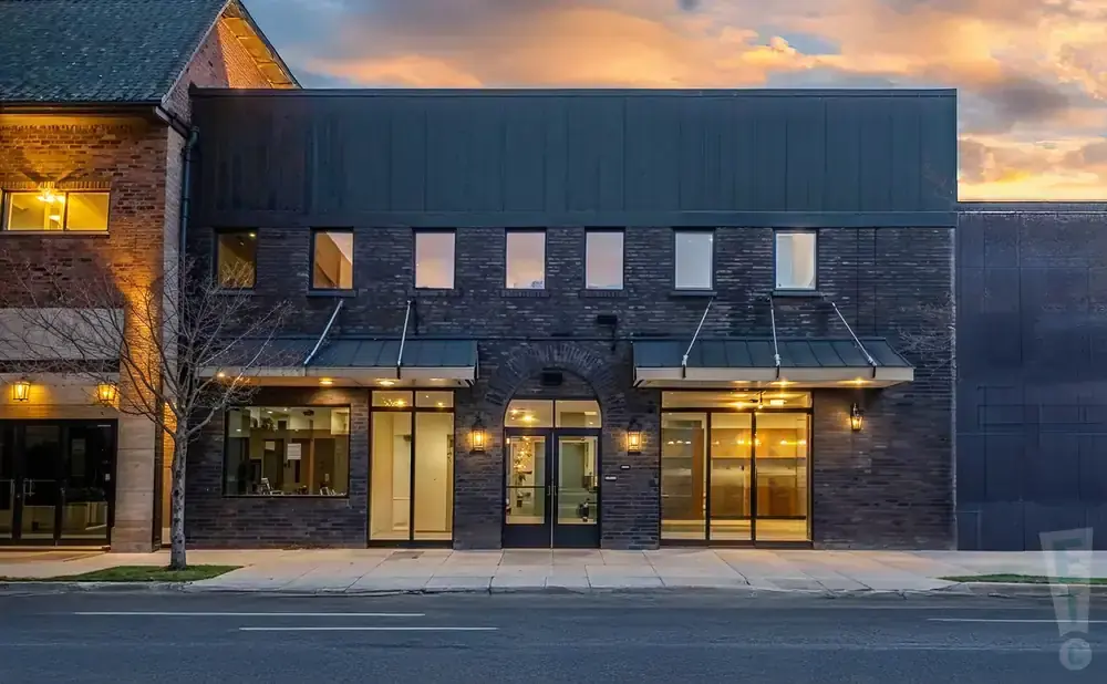 Modern brick building with large glass storefronts and awnings, under a dramatic sunset sky.