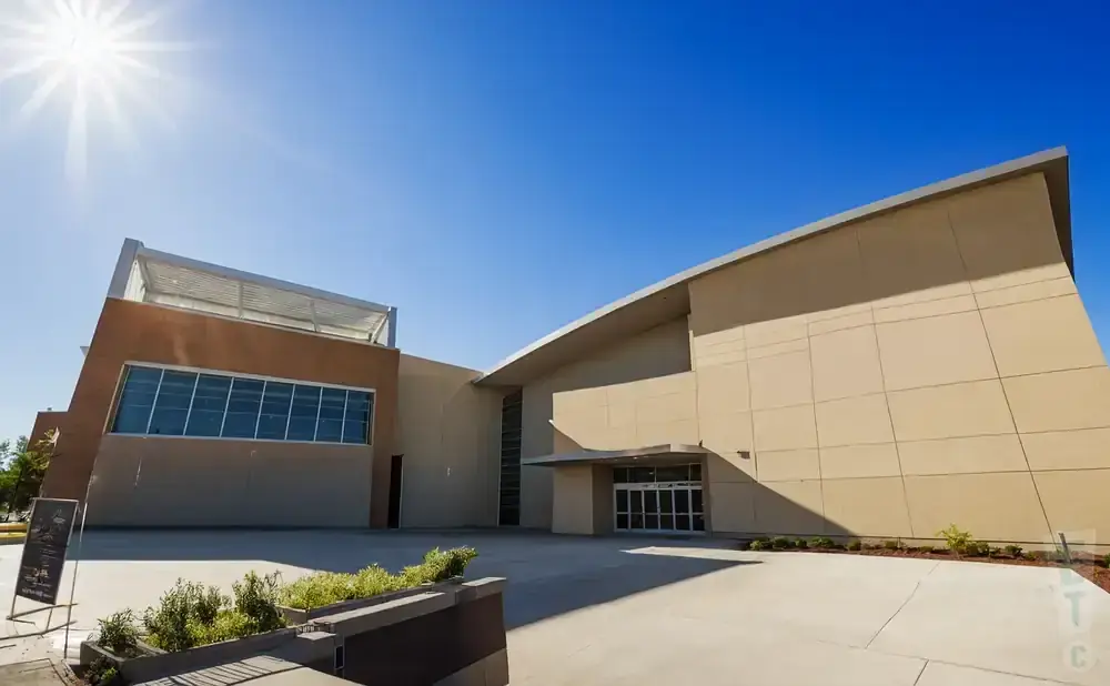 Modern tan building with a large glass entrance and a bright sun in a clear blue sky.