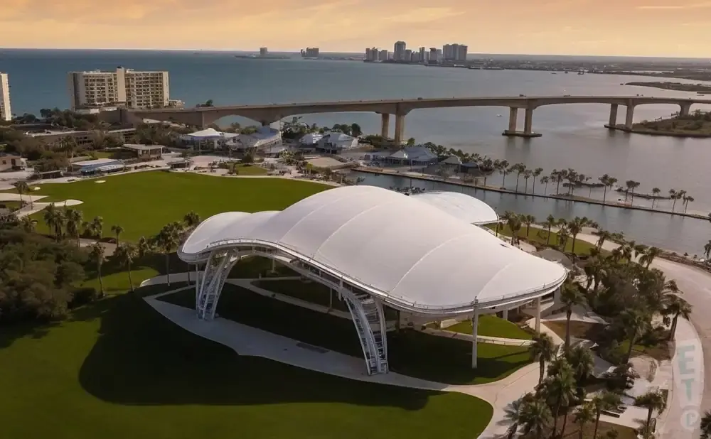 Aerial view of a white-tented amphitheater with a scenic waterfront, bridge, and city skyline in the background.