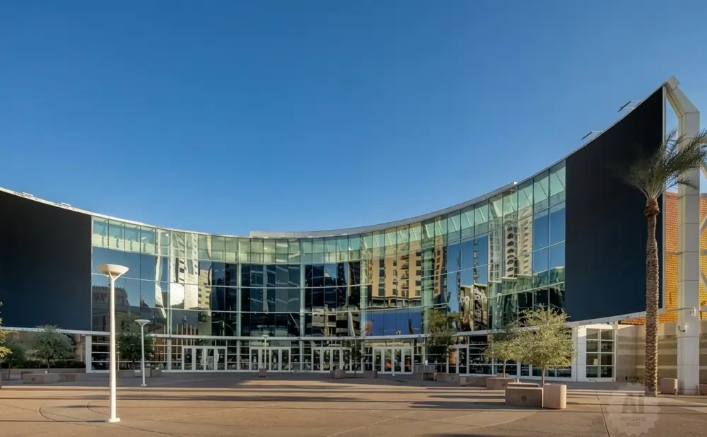 Modern curved glass building with a large black screen facade, reflecting city buildings under a clear blue sky.