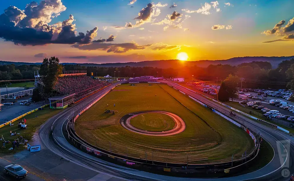 Sunset over a busy race track with grandstands and a large parking lot filled with cars.
