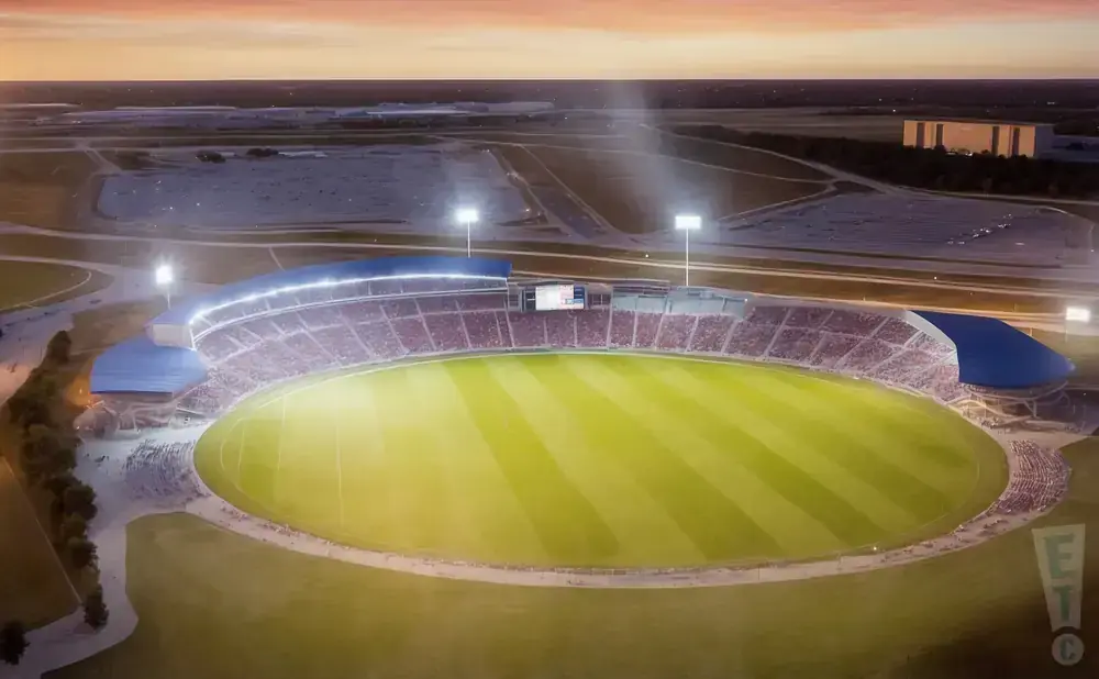 Aerial view of a brightly lit stadium at sunset, with a vast green field and packed stands.