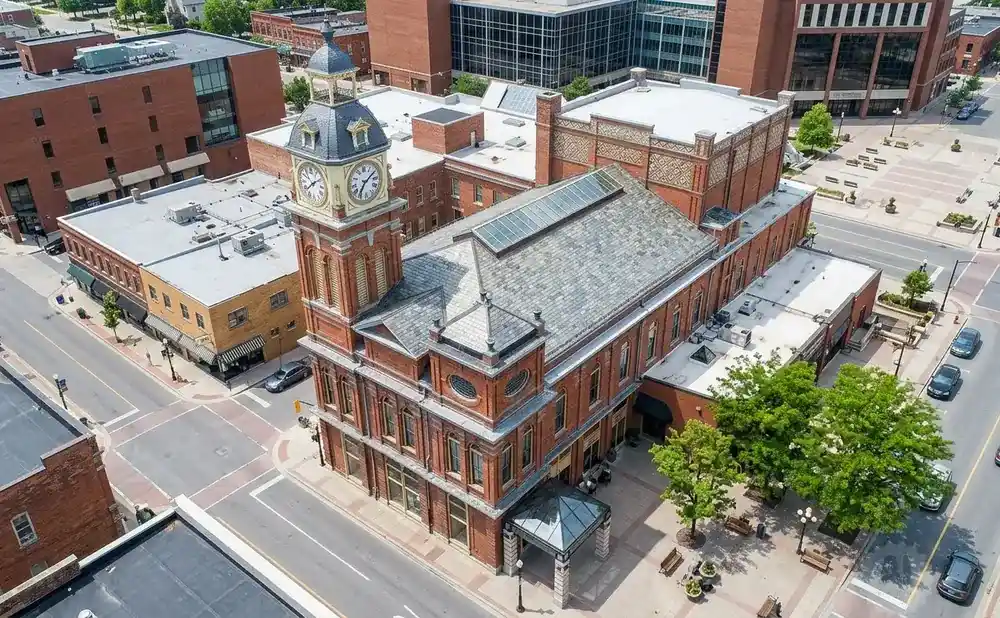 Aerial view of a brick clock tower building in a downtown area with surrounding businesses and street.
