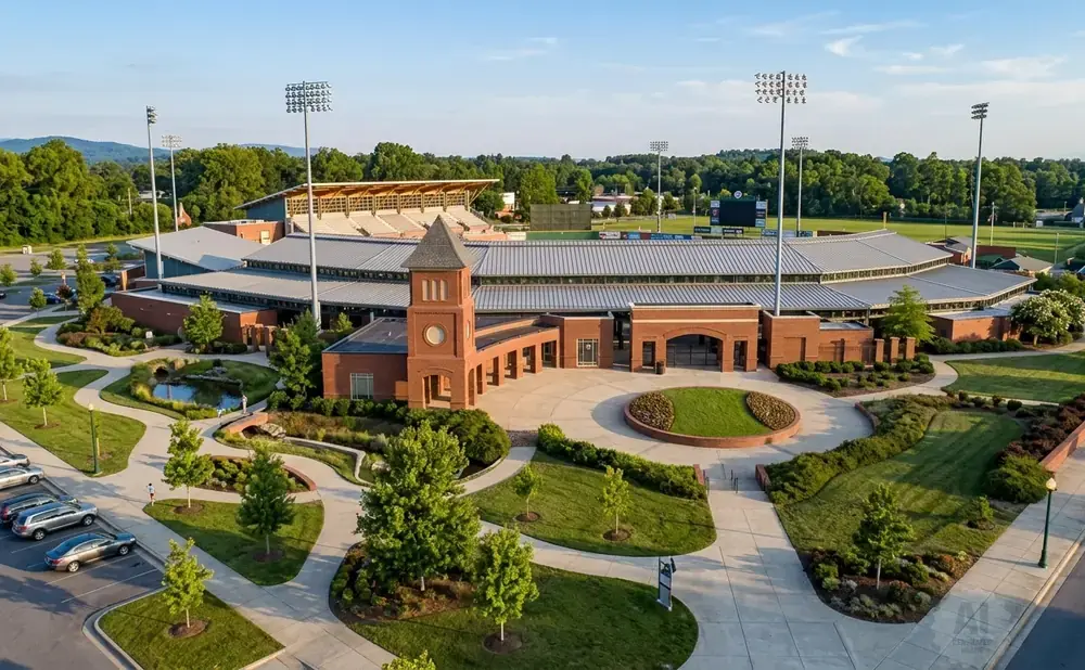 Aerial view of a baseball stadium with brick buildings, tiered seating, and lush green grounds.